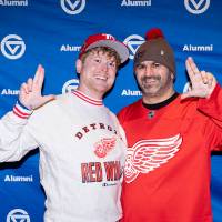 Two GVSU alum giving anchor up sign and smiling in front of backdrop